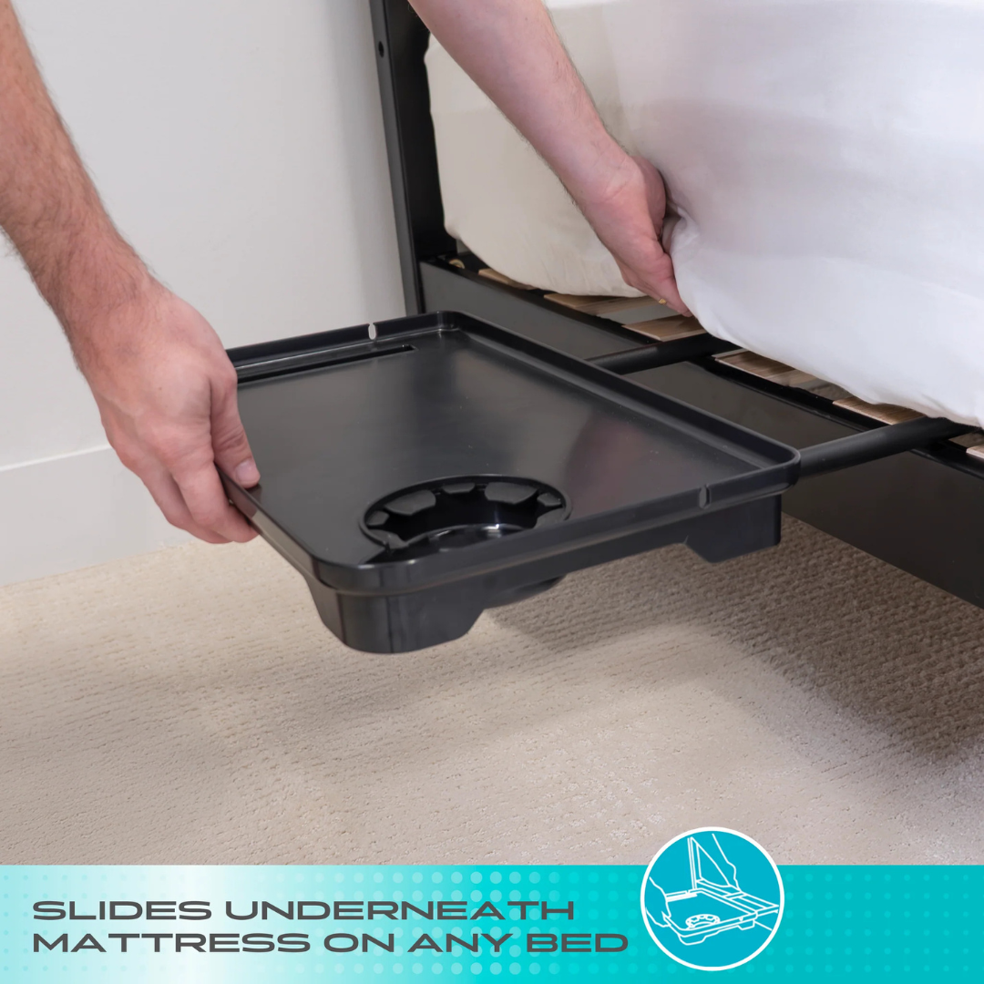A person slides a Stander Wonder Bedside Shelf Tray under the mattress. This space-saving tray with a cup holder fits securely beside any bed. Text reads, Slides underneath mattress on any bed.