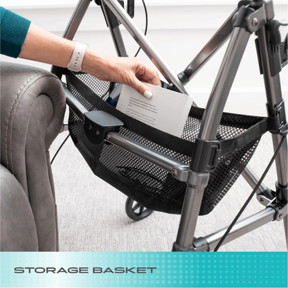 A hand places a book into the black mesh storage basket of the Stander Wonder Indoor Rollator with Tray Table, positioned beside a gray armchair. The text “Storage Basket” appears at the bottom.