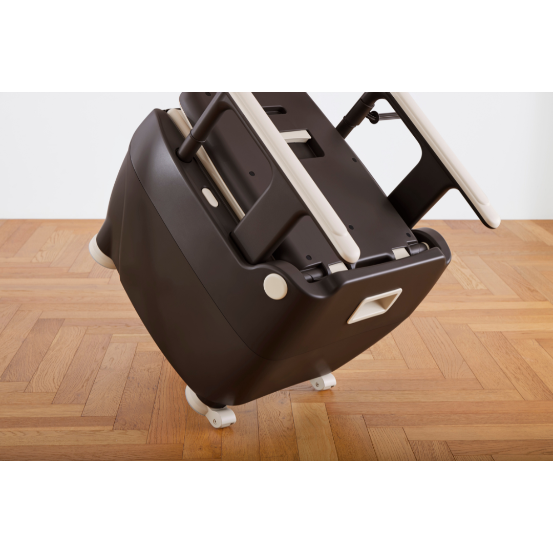 A Wrappon® ORB - Portable Commode Toilet with Auto Waste Sealing, in a sleek black and white design, is shown tilted on its side on a wooden parquet floor, displaying its handles and part of its base.