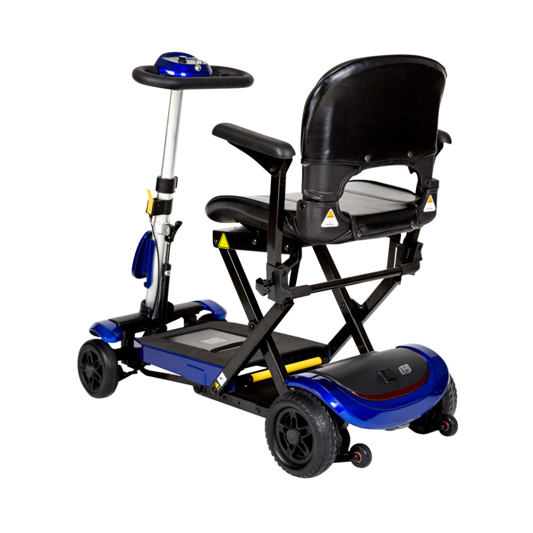 The Drive ZooMe Auto-Flex Folding Travel Scooter is a compact, blue and black 4-wheel scooter with a padded seat, armrests, backrest, and control panel on the handlebar. It’s shown from a rear-side angle.