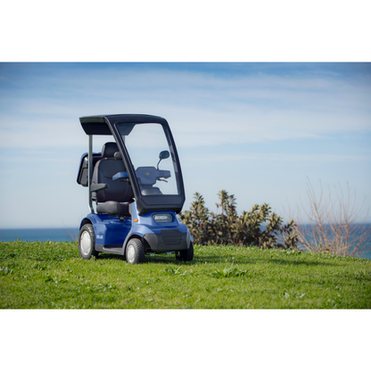 A small, blue Afikim Afiscooter Solar - Solar-Powered Bariatric Mobility Scooter with Canopy sits on a grassy hill by the ocean. The clear sky is dotted with a few clouds. Nearby bushes enhance its eco-friendly charm, portraying tranquility and cutting-edge mobility innovation.