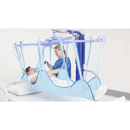 A healthcare worker uses the ARJO Maxi Move Electric Floor Lifter & All-Purpose Patient Lift to safely transfer a patient in a blue sling above a hospital bed. The caregiver smiles as they assist, and the patient looks calm during the process.