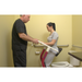 A healthcare professional assists a woman using the Bestcare STA400 Standing Transfer Aid in a bathroom with light yellow walls and grab-bar-equipped toilet. The woman securely holds the device while they both focus on ensuring her safety during the transfer process.