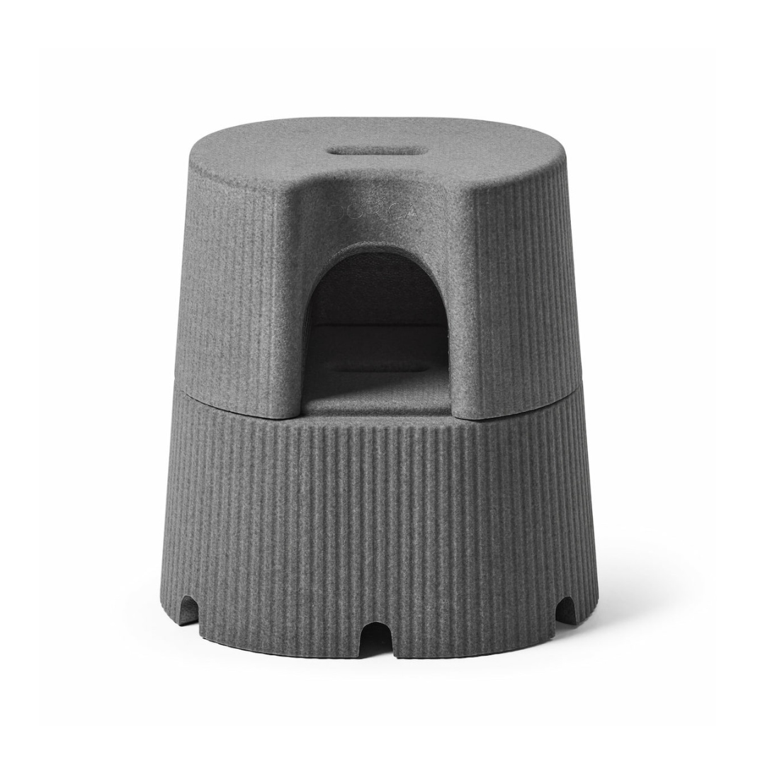 The byACRE DORICA – Versatile Step Stool & Seat is a modern gray, cylindrical design with a built-in handle, ribbed sides, and an arched middle compartment for storage. Water-resistant and anti-slip for reliable use as seat or footrest.