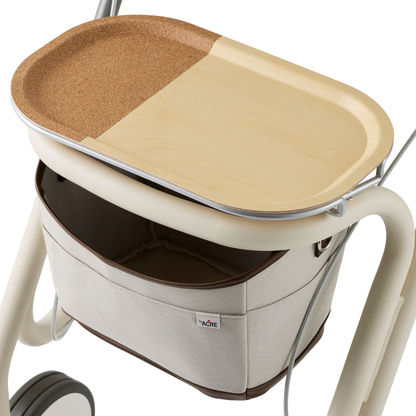 The byACRE Scandinavian Butler At-Home Rollator is a modern mobility aid with a beige fabric basket, sleek metal frame, and a wooden tray featuring a partial cork surface.