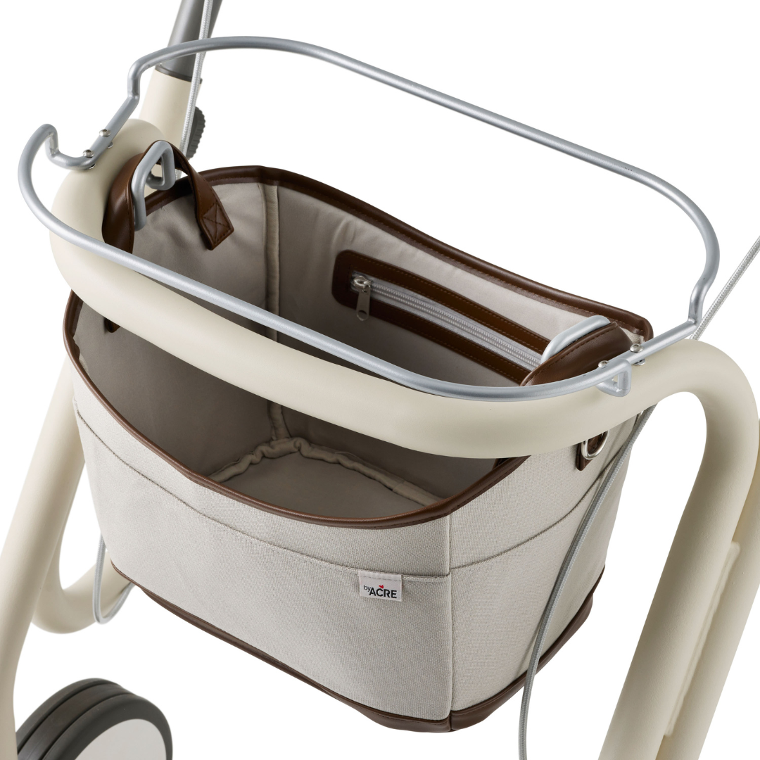 A close-up of a beige byACRE Scandinavian Butler At-Home Rollator shows its fabric storage basket with brown trim and a zippered pocket, empty and neatly attached to the walker frame.