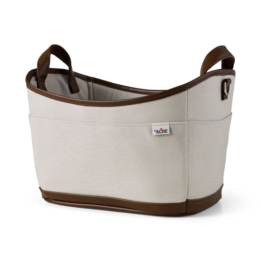 The byACRE Scandinavian Butler At-Home Rollator features a beige fabric basket with brown leather handles and trim, an outer pocket, a small side label, and an oval structured design inspired by Scandinavian style.