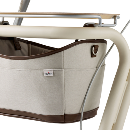 Close-up of a beige fabric storage basket with brown trim, hanging from the byACRE Scandinavian Butler At-Home Rollator’s cream metal frame. A small TACRE label on the side highlights its Scandinavian-inspired design.