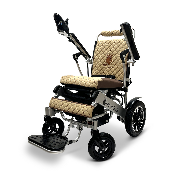 The ComfyGo MAJESTIC IQ-8000 Remote Controlled Lightweight Electric Wheelchair boasts a sleek, modern design that is perfect for travel. It features beige quilted cushions, a lightweight black frame, a joystick controller mounted on the armrest, and large rear wheels to ensure stability. The brand name Majestic is prominently displayed on the backrest.