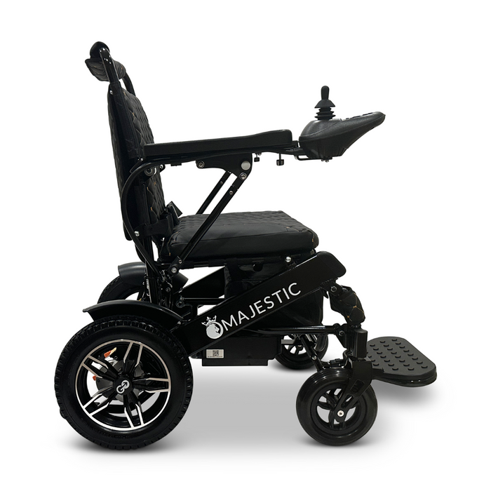 Side view of the ComfyGo MAJESTIC IQ-8000 Remote Controlled Lightweight Electric Wheelchair in black, featuring a joystick control on the right armrest. The travel-friendly design includes large rear wheels, a padded seat, and a footrest, with the brand name "Majestic" visible on the side.