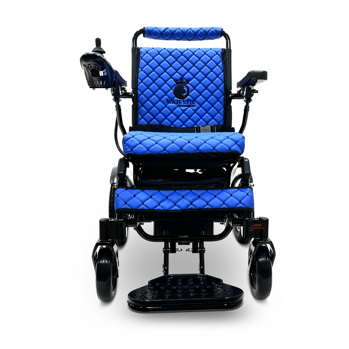 The ComfyGo MAJESTIC IQ-8000 is a lightweight electric wheelchair in blue, featuring quilted seat and backrest upholstery. It includes a joystick control mounted on the right armrest and has two large rear wheels complemented by smaller front wheels for easy travel. The Majestic brand name is prominently displayed on the backrest.