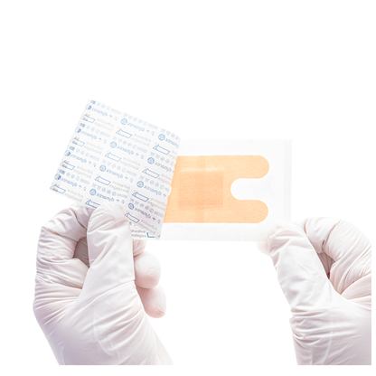 Gloved hands hold a transparent Dynarex DynaSafety Adhesive Fabric Bandage with an orange pad, partially peeled from its paper backing, against a white background.