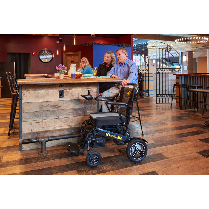 Man sitting at the bard with the Golden Tech Stride Folding Lightweight Powerchair in the front of the bar