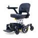 The Golden Tech GP130 Buzzaround CarryOn is an ultra-compact black electric wheelchair featuring a comfy cushioned seat with armrests, joystick control on one armrest, 4-wheel suspension for smooth rides, and a small basket underneath.