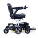 The Golden Tech GP130 Buzzaround CarryOn Portable Powerchair is an ultra-compact, sleek black folding wheelchair with joystick controls on the right armrest. It features a cushioned seat and backrest, a storage basket below, four suspension wheels, a footrest, and a modern design.