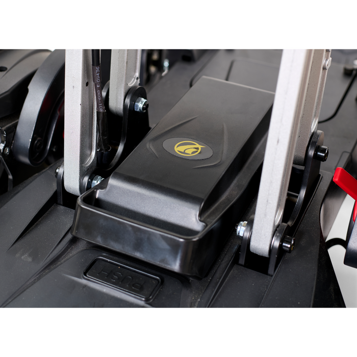Close-up of the foot pedal area on a Golden Tech GP130 Buzzaround CarryOn Portable Powerchair, showing a black pedal with a yellow logo and surrounding metal supports. The ultra-compact design includes a PUSH label and a red release lever on the right, similar to precise 4-wheel suspension systems.