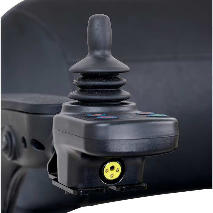 Close-up of the joystick control panel on a Golden Tech GP130 Buzzaround CarryOn Portable Powerchair, featuring a central stick and colored indicator buttons. The blurred background highlights the joysticks details and advanced 4-wheel suspension system.