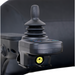 Close-up of the joystick control panel on a Golden Tech GP130 Buzzaround CarryOn Portable Powerchair, featuring a central stick and colored indicator buttons. The blurred background highlights the joysticks details and advanced 4-wheel suspension system.