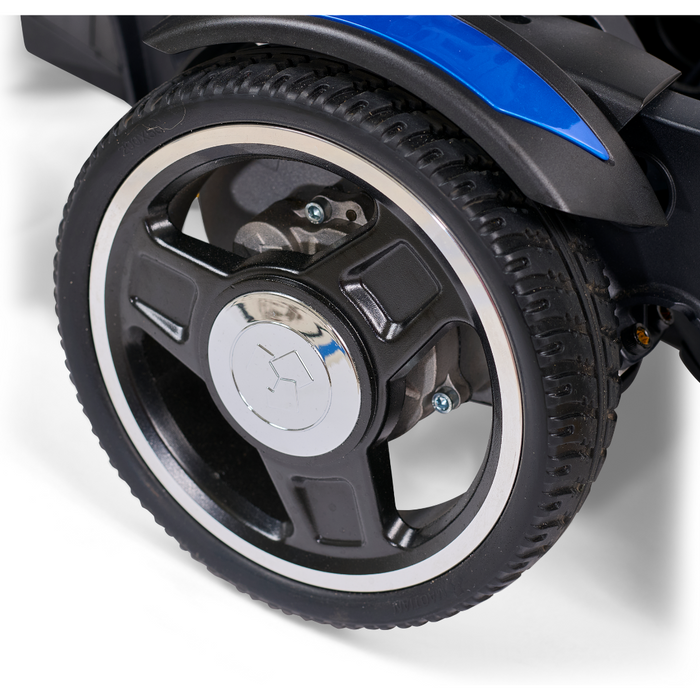 Close-up of a five-spoke black wheel with a silver hub on the Golden Tech GP130 Buzzaround CarryOn Portable Powerchair. The surrounding parts feature black and blue colors. The tires tread pattern is clear, suggesting its new or barely used.