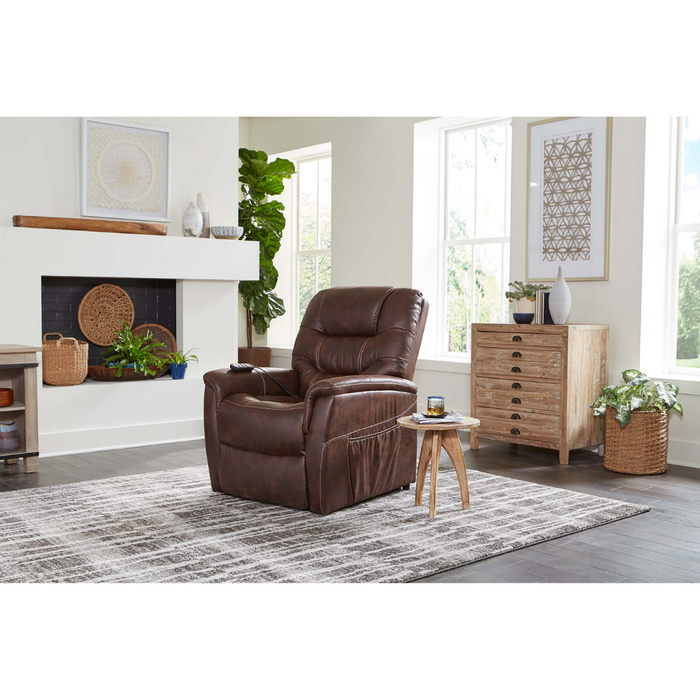 A cozy living room has a brown Golden Tech PR446 DeLuna™ Dione Recliner with Lift Assist on a striped rug. A wooden side table is beside it, near a textured cabinet and fireplace adorned with plants and decor. Large windows fill the space with natural light.