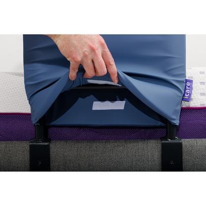 A hand lifts a blue cover to reveal an icare tag on the mattress, showing purple, white, and gray inner layers—highlighting the iCare Medical Bed Safety Rails for fall prevention and added bedside support.