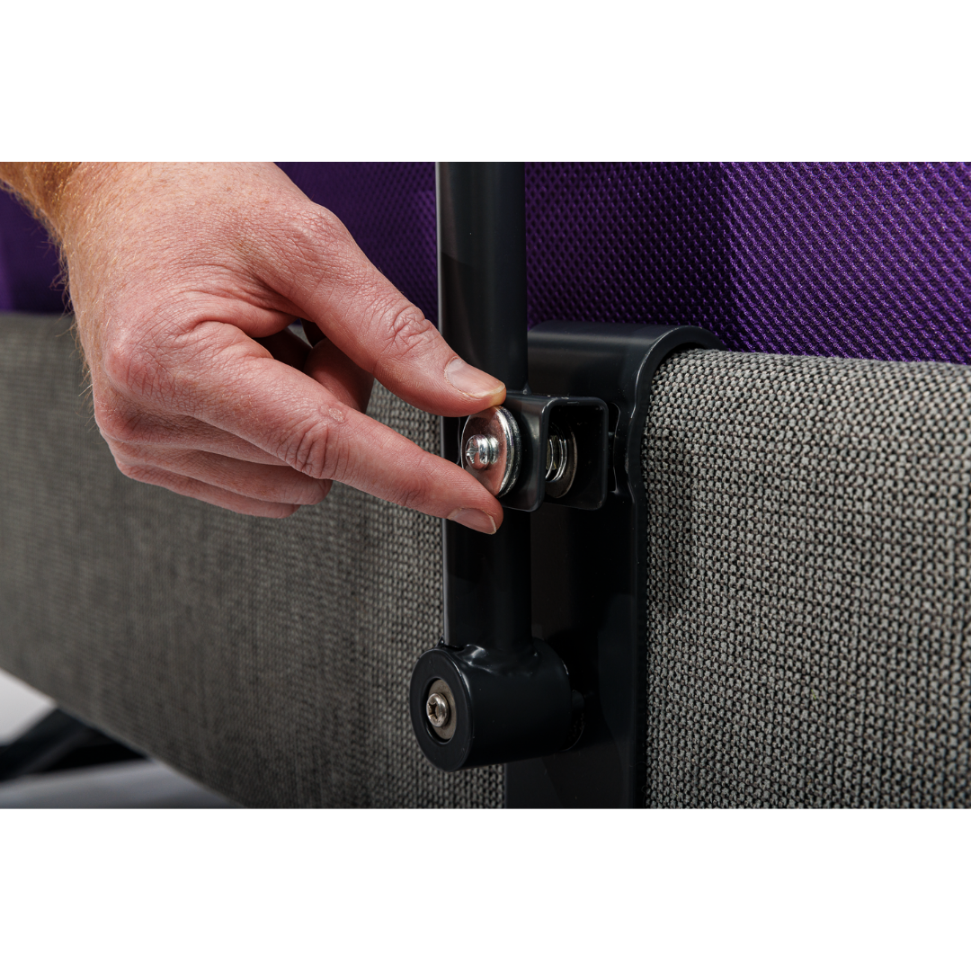 A close-up of a hand adjusting a bolt on the iCare Medical Bed Safety Rails, attached to a black metal frame with gray upholstered bed base and purple mattress, enhancing fall prevention and safety.