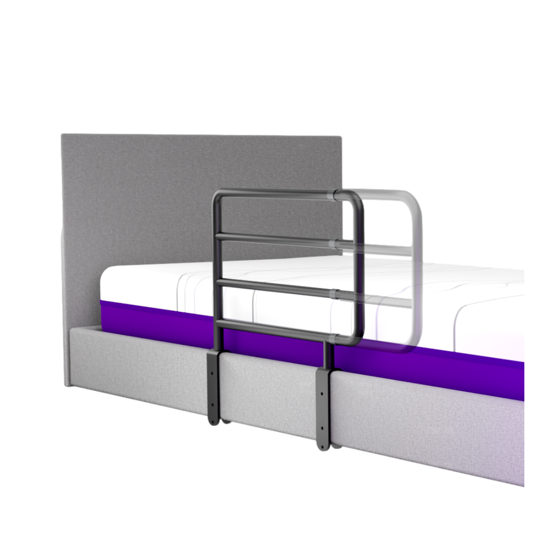 A grey upholstered bed with headboard features iCare Medical Bed Safety Rails attached to the side for fall prevention and support; the mattress includes a distinctive purple layer.