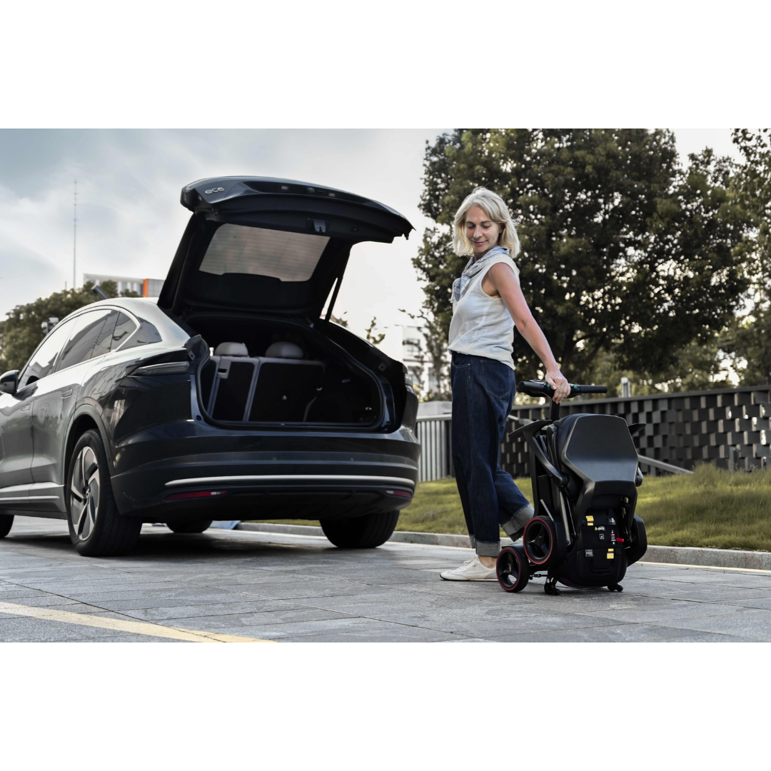 A woman stands beside a car with an open trunk, holding a folded iMOVE AirCarbon Folding Carbon Fiber Scooter.