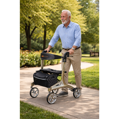 An older man with gray hair and a beard smiles while walking outside on a paved path using the Rhythm Arpeggio Folding Portable Rollator with XL 8" Wheels in Champagne, which features a black storage bag. Green trees and shrubs are behind him.