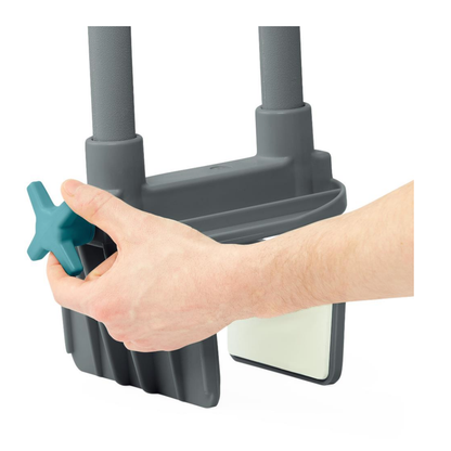 A hand twists a teal knob on the Medline Deluxe Bathtub Grab Bar with Microban in light gray, which features two vertical handles and a white non-slip, antimicrobial panel for added safety.