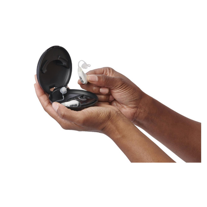 A persons hands hold a Medline Rechargeable Digital OTC Hearing Aid case with one hearing aid inside and another—featuring built-in volume control—held above the open case, both shown against a white background.