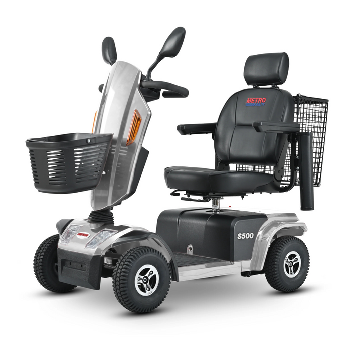 The Metro Mobility S500 Heavy Duty 4-Wheel Power Scooter has a silver color, black cushioned seat with armrests, and backrest. It features rear and front wire baskets, handlebars with controls, for strong support.