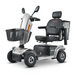 The Metro Mobility S500 Heavy Duty 4-Wheel Power Scooter has a silver color, black cushioned seat with armrests, and backrest. It features rear and front wire baskets, handlebars with controls, for strong support.
