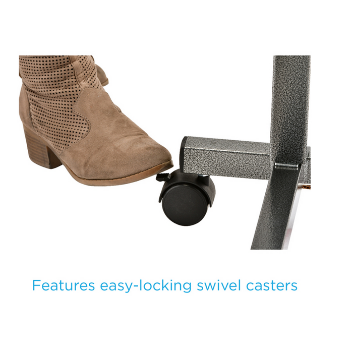 A Brown suede boot presses on a wheel lock of a metal frame featuring easy-locking swivel casters and adjustable height for the Nova Medical Rolling Overbed Table with Tilting Tray.