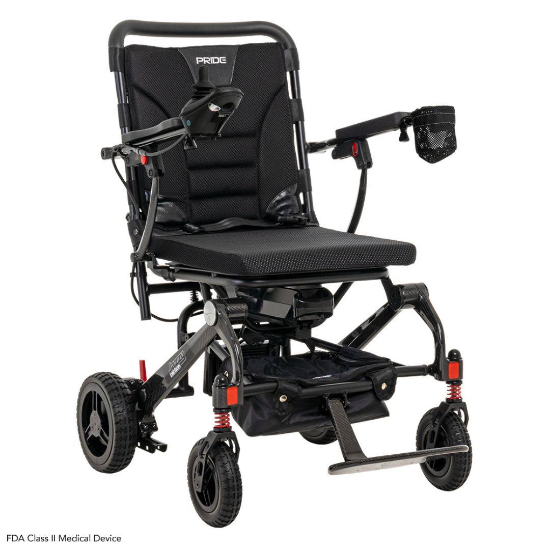 The Pride Mobility Jazzy® Carbon Ultralite Powerchair is a lightweight black electric wheelchair styled with padded seat and armrests, right-side joystick control, large rear and anti-tip front wheels, and a storage pouch—ideal as a travel power chair.