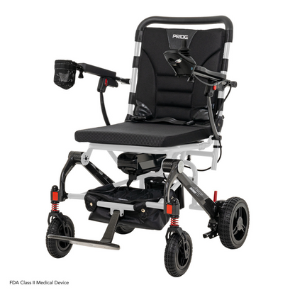The Pride Mobility Jazzy® Carbon Ultralite Powerchair is a sleek, lightweight travel power chair featuring a black seat, armrests, footrest, small front wheels, larger rear wheels with red shock absorbers, and an airline-compliant lithium battery. It includes a removable joystick with USB charger for added convenience.
