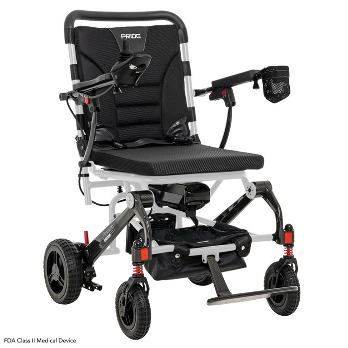 The Pride Mobility Jazzy® Carbon Ultralite Powerchair is a black and silver travel chair with cushioned seat, armrests, footrest, small front wheels, larger rear wheels, and a detachable joystick with USB charger. It includes a mesh cup holder and is labeled FDA Class II Medical Device.