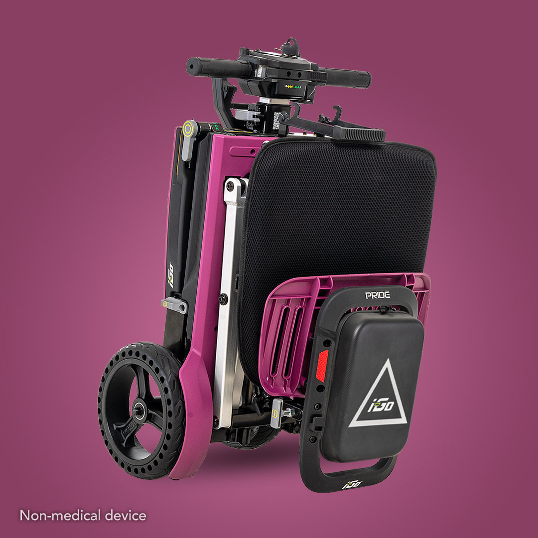 Pride Mobility i-Go™ Portable Travel Scooter folded on a purple background, showcasing an ultra-compact design with black and pink components, a small control panel on the handlebar, and large rear wheels. Text reads: Non-medical device.