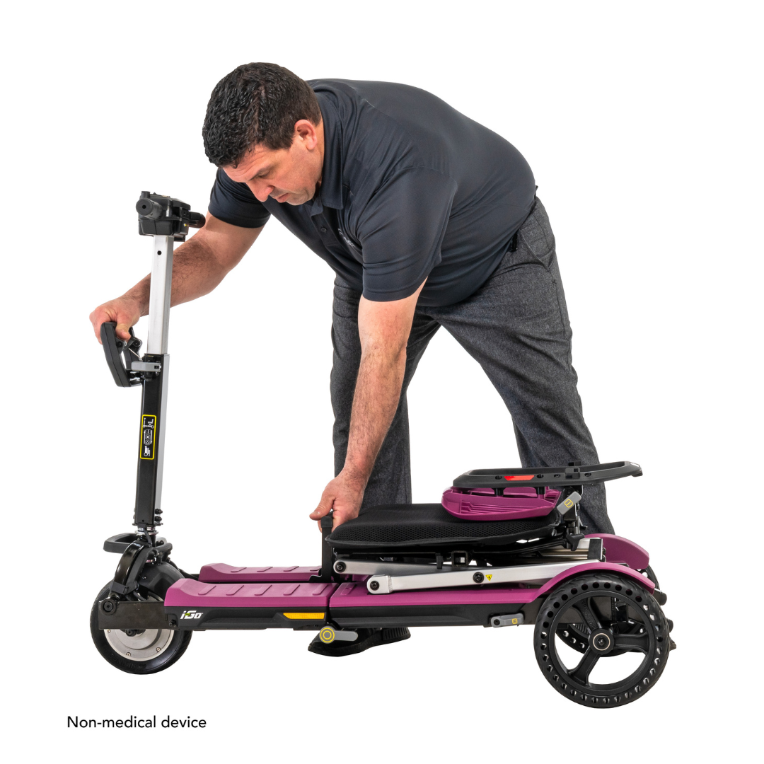 A man in a dark shirt and gray pants is adjusting a Pride Mobility i-Go™ Portable Travel Scooter with an ultra-compact profile. The scooter has a small seat, three wheels, and features feather-touch disassembly. The text reads Non-medical device.
