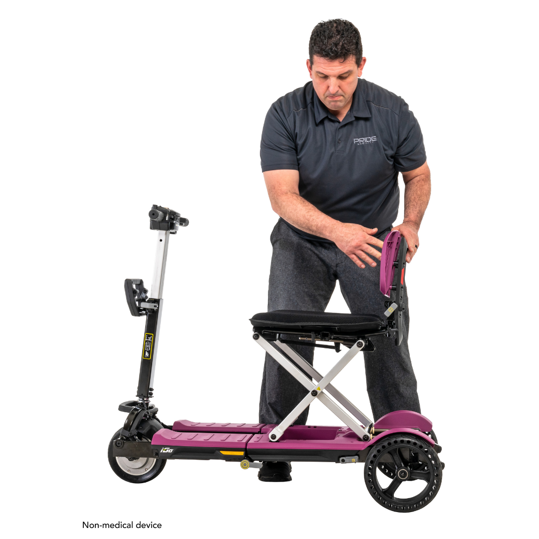 A person demonstrates folding the Pride Mobility i-Go™ Portable Travel Scooter with feather-touch disassembly. Its ultra-compact profile features three wheels and a handlebar, and the crouched individual highlights its ease of use against a white background. Text reads Non-medical device.
