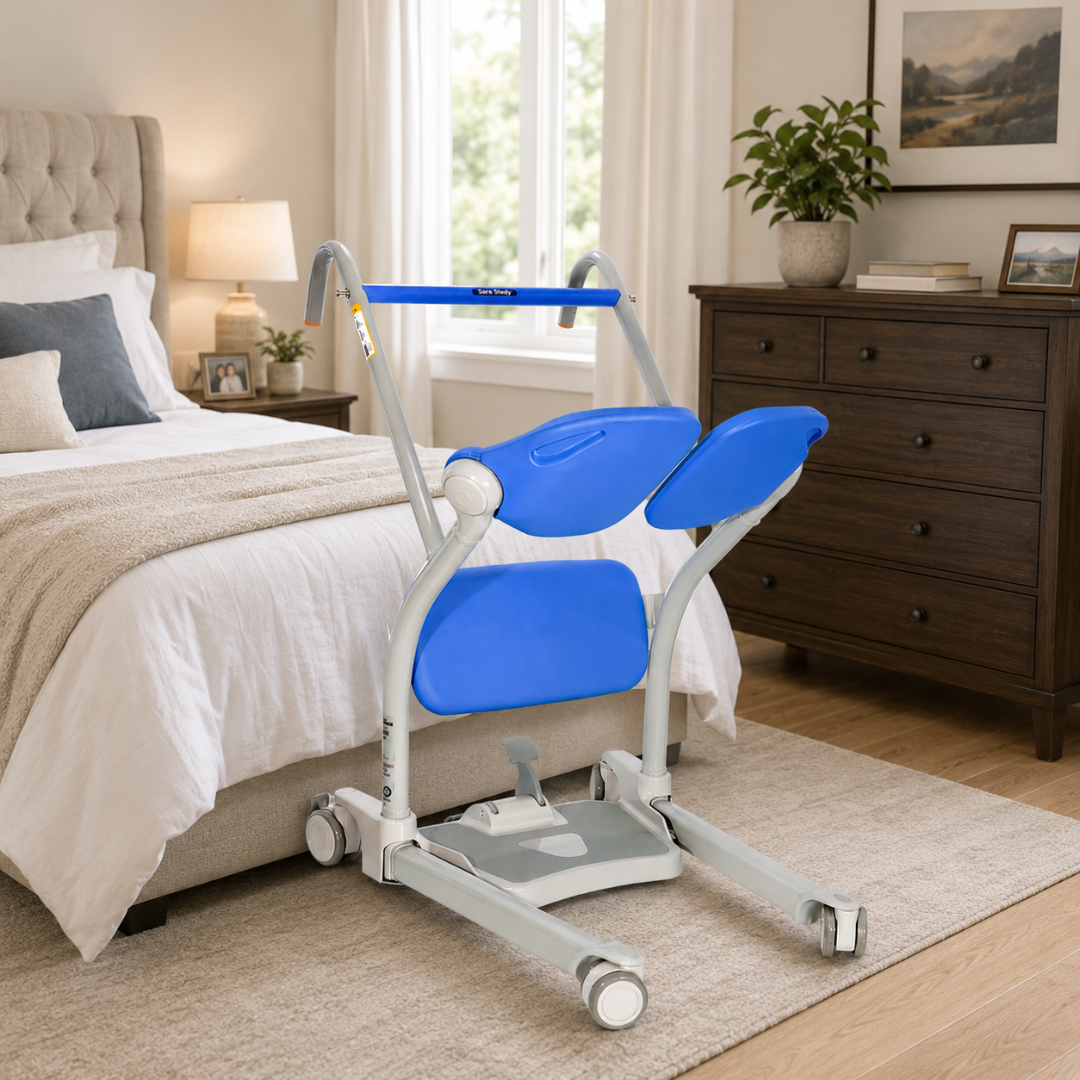 An ARJO Sara Stedy Manual Standing Aid & Sit-To-Stand Transfer Lift with blue and gray colors and wheels is placed beside a neatly made bed in a cozy, well-lit bedroom featuring wooden furniture and decor.