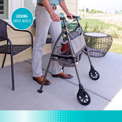 A person stands on a porch holding the Signature Life Elite Bariatric Travel Walker with large locking swivel wheels and a storage pouch, next to a chair and outdoor furniture.