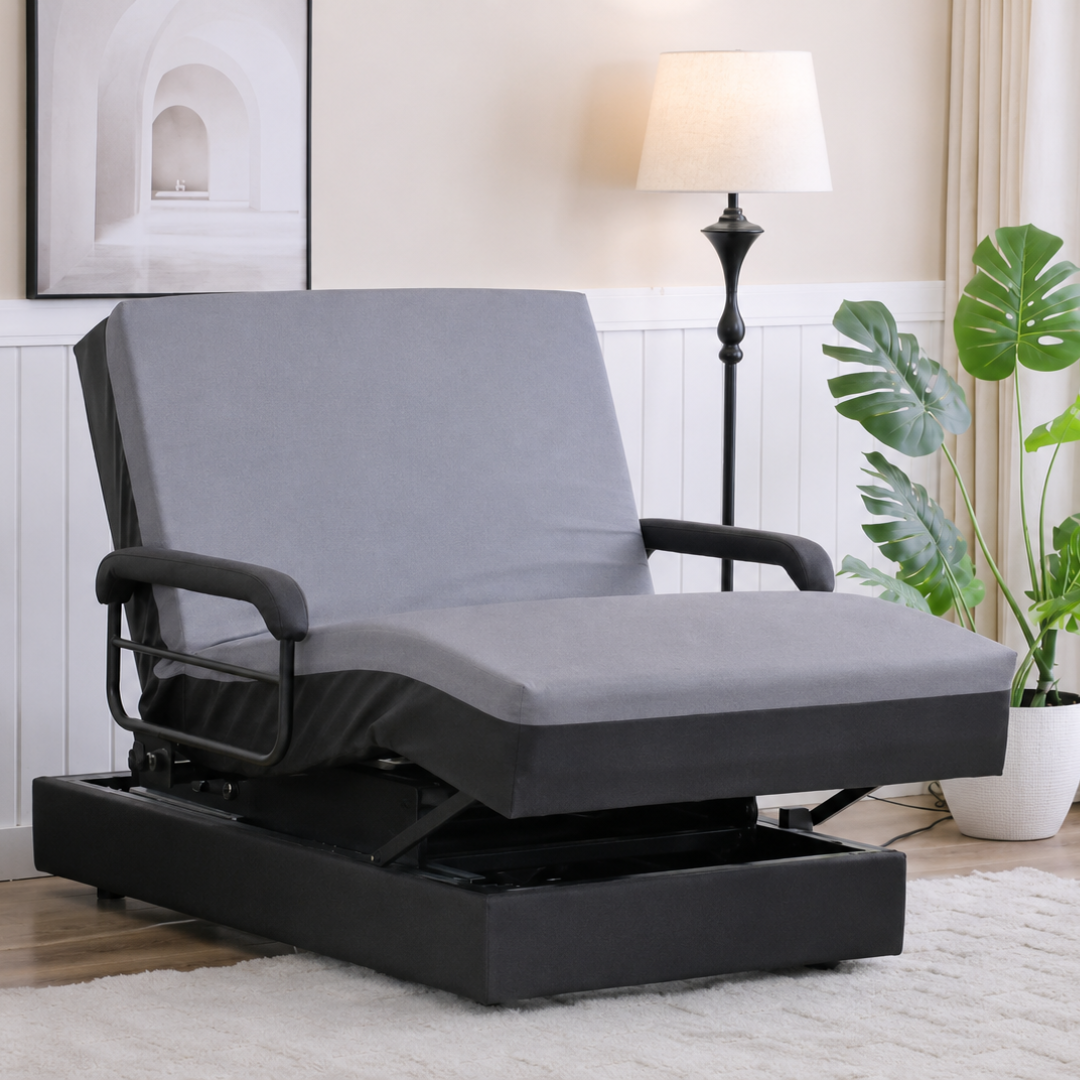A modern gray adjustable chair with black armrests sits in a cozy living room with a tall lamp, potted plant, and wall art—perfect for added comfort and style beside your EZLift Bed Hi-Lo Pro™ Electric Bed with Stand Assist.