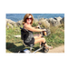 A woman in sunglasses rides her SmartScoot® Ultra Light Mobility Scooter - FAA Approved along a rocky shoreline, her gray tank top and shorts catching the breeze as she glides effortlessly, savoring views of blue water and grassy terrain.