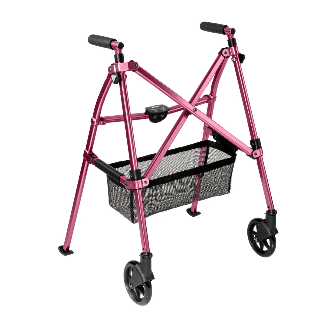 The Stander Bariatric Wonder Walker Plus with Wheels is a compact, metallic pink folding walker featuring two front wheels, black hand grips, and a black mesh storage basket between the legs.