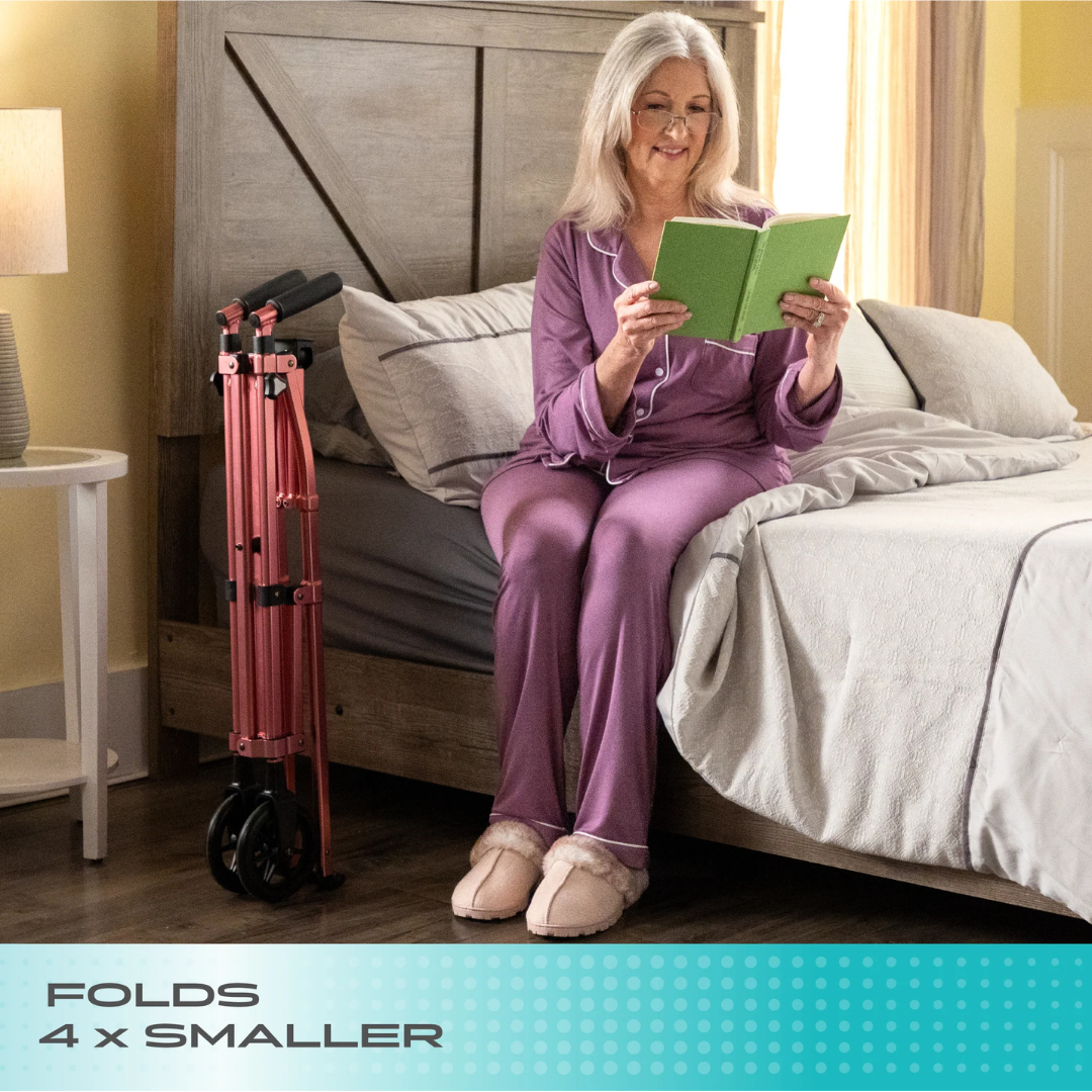 A smiling older woman in purple pajamas sits on a bed reading. Next to her, a Stander Bariatric Wonder Walker Plus with Wheels is folded, highlighting its compact size. Text reads: FOLDS 4x SMALLER.