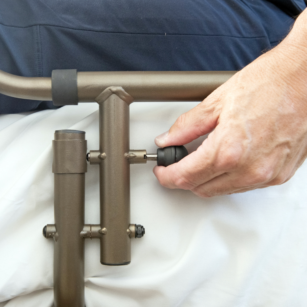 A close-up shows a hand adjusting the black knob on the Signature Life Sleep Safe Extendable Bed Rail, with part of a leg resting on white sheets. Warranty details and specifications are available upon request.