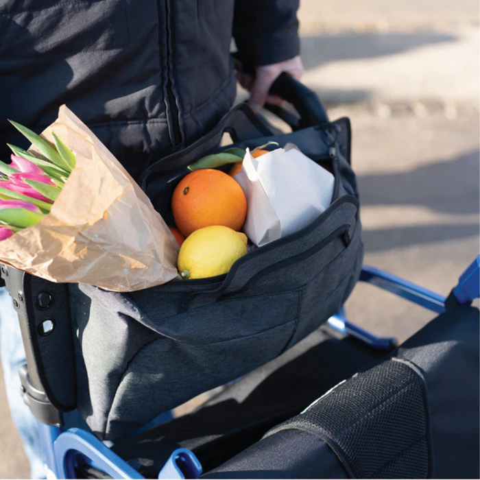 Someone uses a Strongback Mobility SEATA Ergonomic Rollator with a black bag holding pink tulips, an orange, lemon, and a paper-wrapped item. The lightweight rollator glides smoothly as they enjoy the sunny day outside.