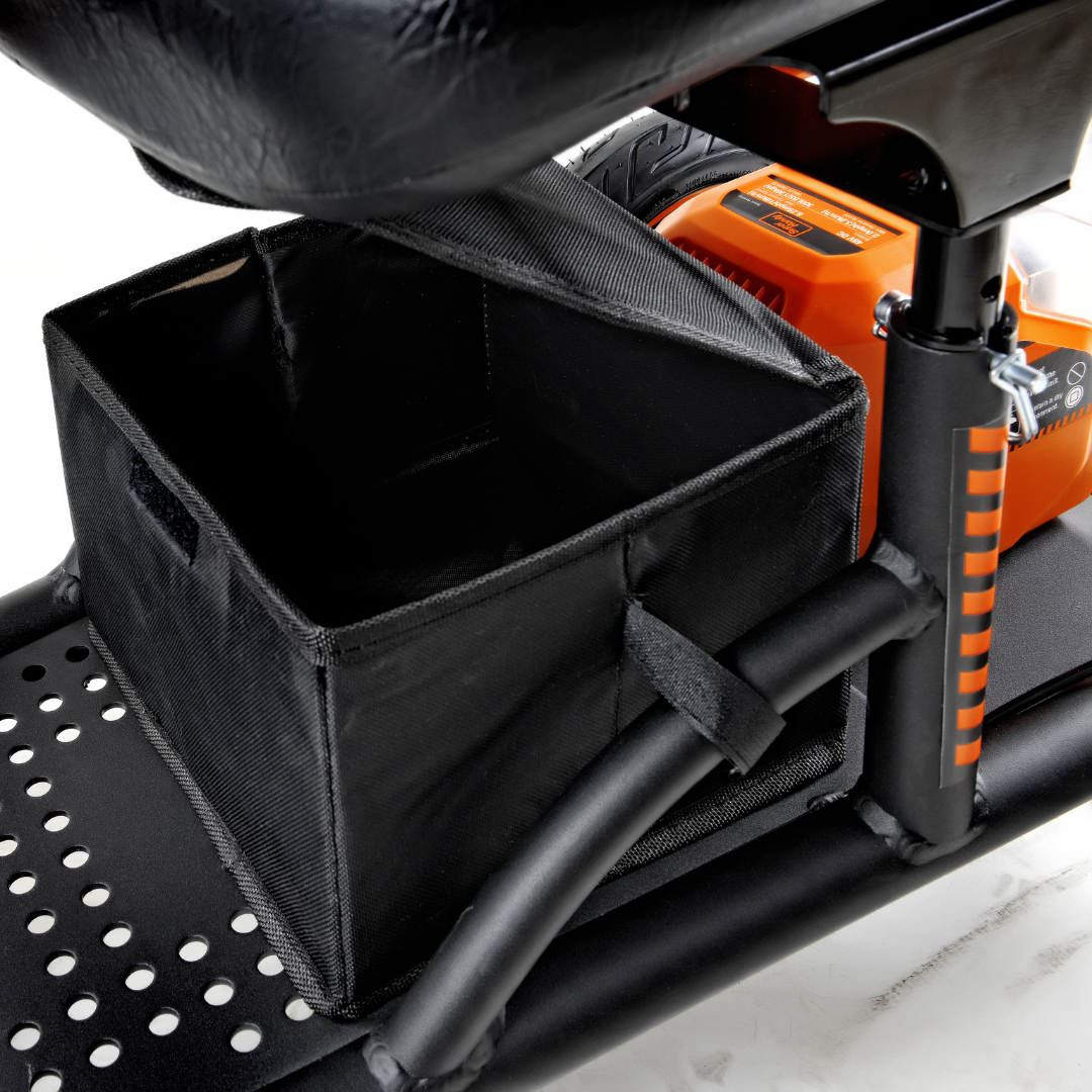 Close-up of a black storage box on the floorboard of a SuperHandy Explorer Portable Power Mobility Scooter, featuring durable pneumatic wheels, perforated footrests, and orange-accented suspension spring. The empty box shows part of the seat and handle.