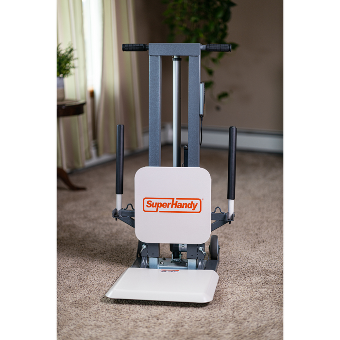 Image of the SuperHandy GoRise FS, a bariatric electric lift assistant with a metal frame and dual black handles on carpeted flooring. It features a wide white base supporting up to 500 lbs for excellent mobility aid. A potted plant and curtains are in the background.
